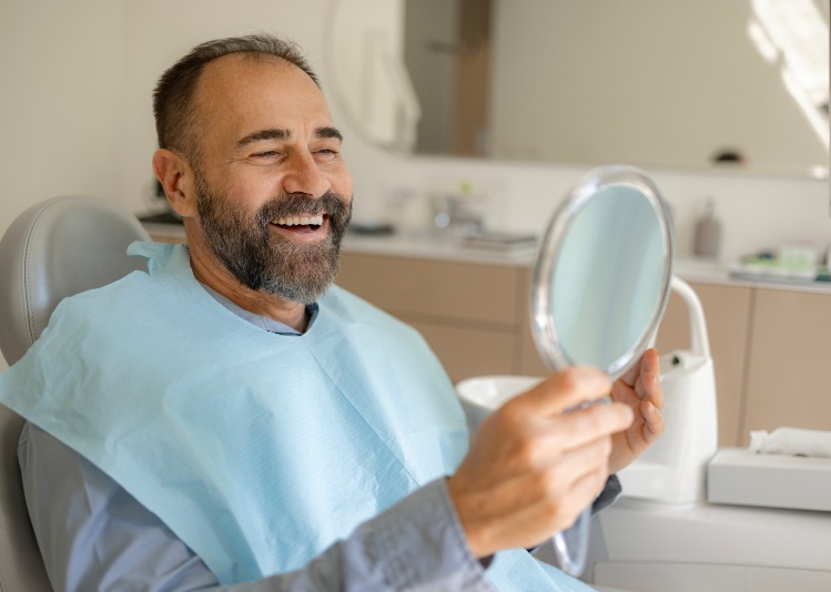 An adult man looking at his teeth after getting restorative dentistry services in Wyoming, MI